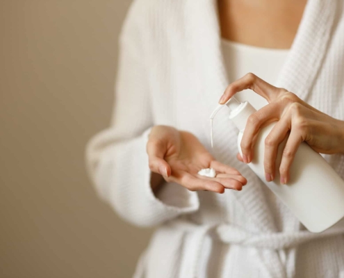 Woman Wearing Robe Putting Moisturizer in Hand