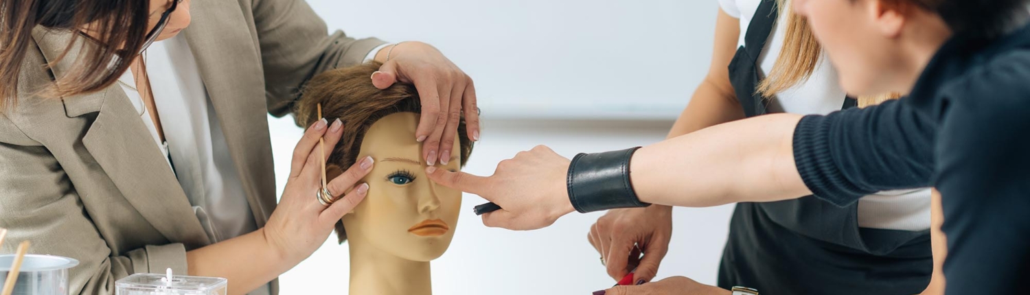 Side View Of A Group Of People Practicing On A Mannequin Head In Cosmetology School 1500x430.jpg.jpg