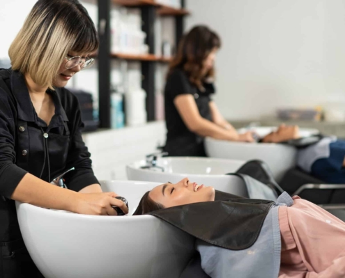 Side view of a stylist washing a woman's hair in salon station